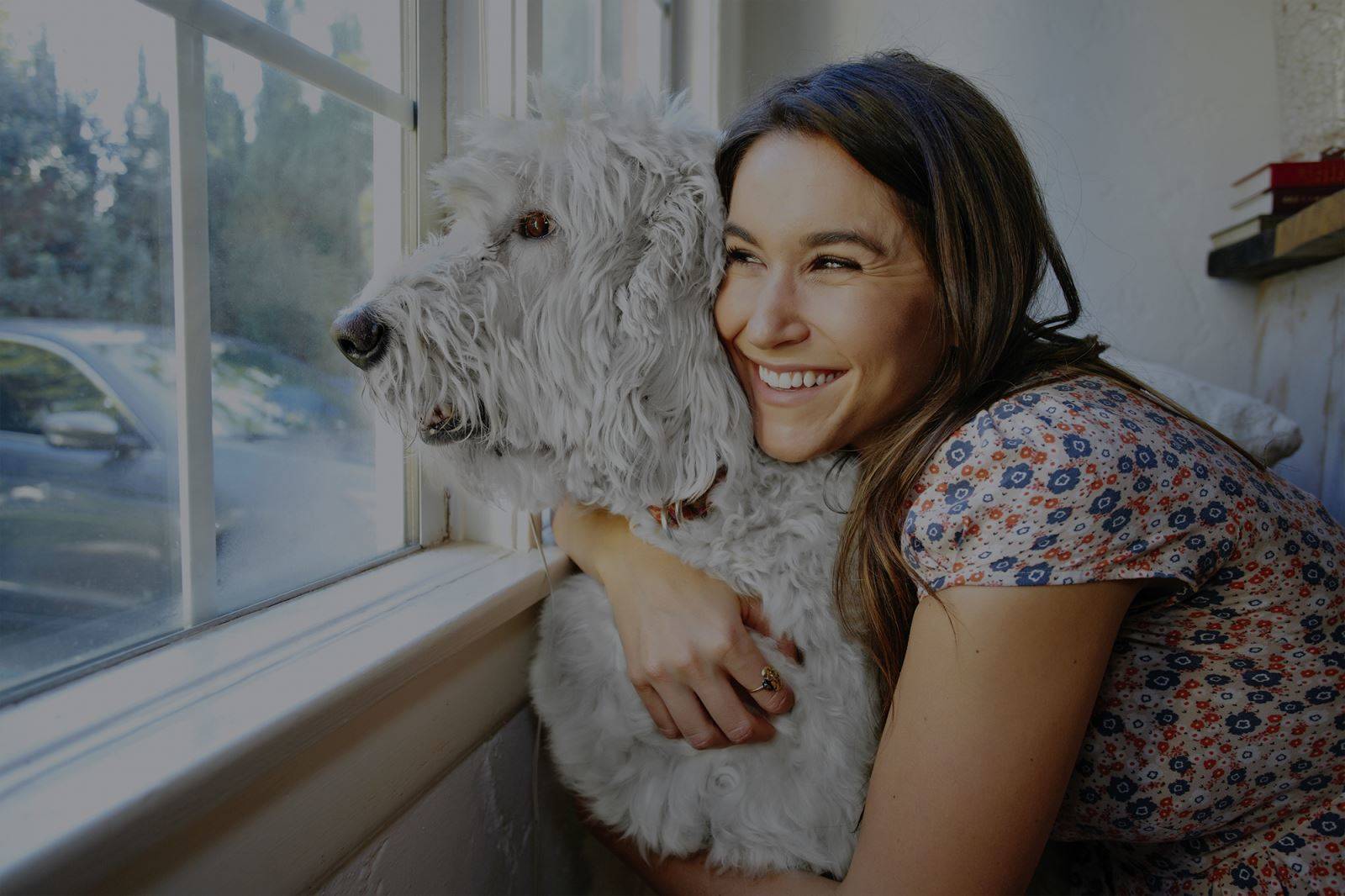 Female hugging dog looking out of window