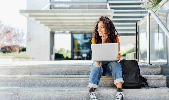 woman sitting on stairs outside of building with a laptop on her lap