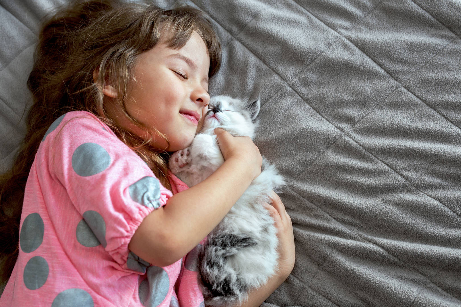 Smiling girl and little cat lying down on the bed.